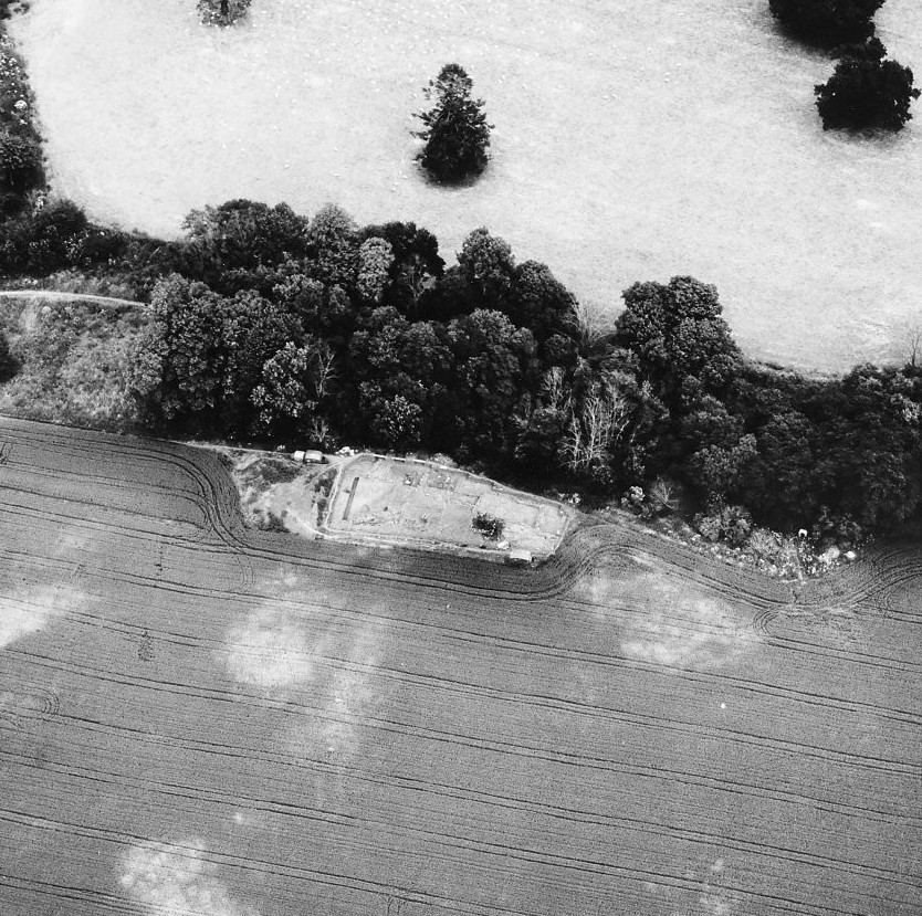 aerial photograph of excavation area within field, next to trees. In black and white