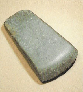 Photograph of stone axehead, oblique, on a beige background