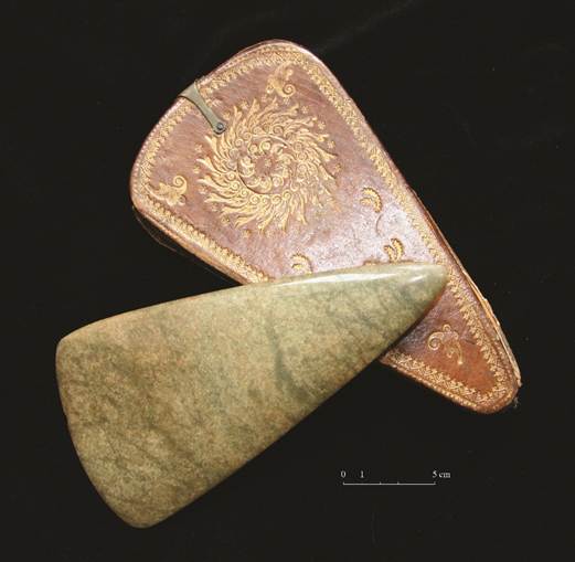 polished stone axehead positions on top of a decorated carrying case on  black background