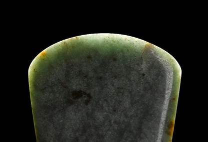 top edge of an axehead with light on it, against a black background