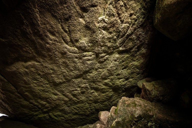 A dark image taken inside a cairn, using torchlight to show the carvings that resemble a red deer.