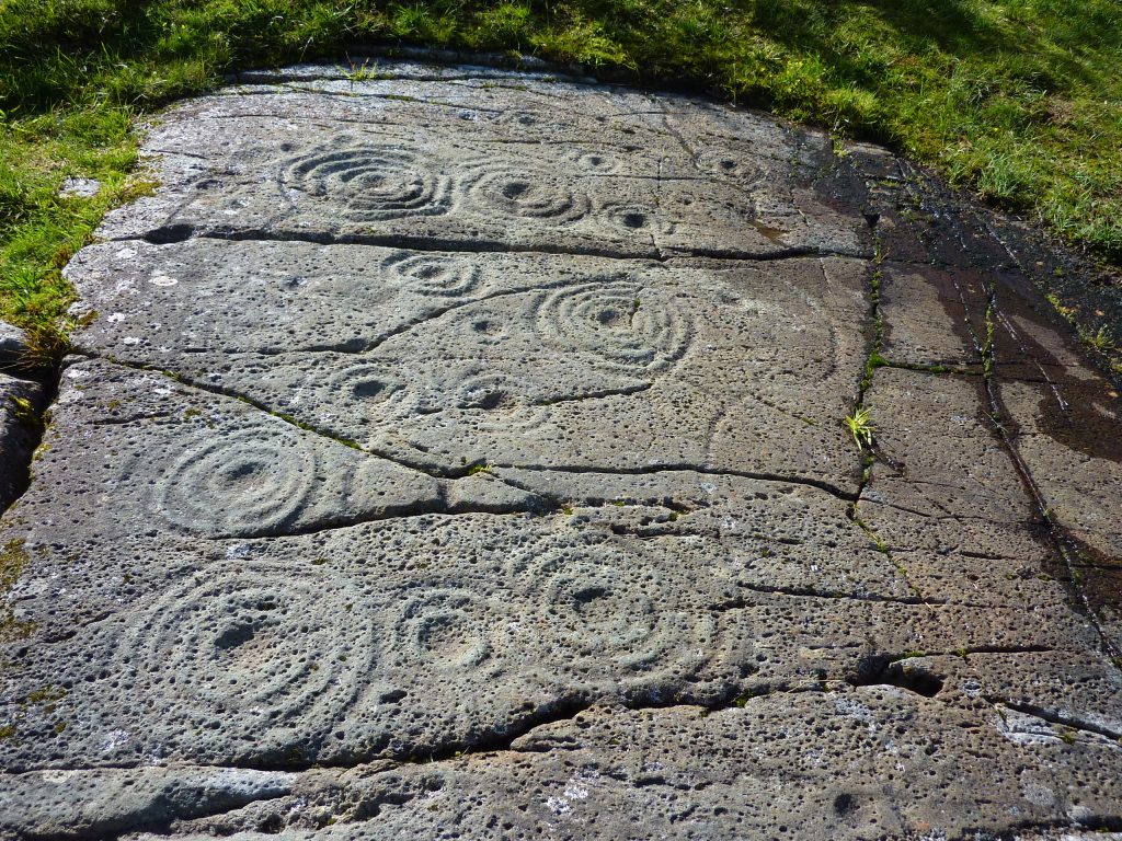 Large, flat rock art in a grassy landscape.