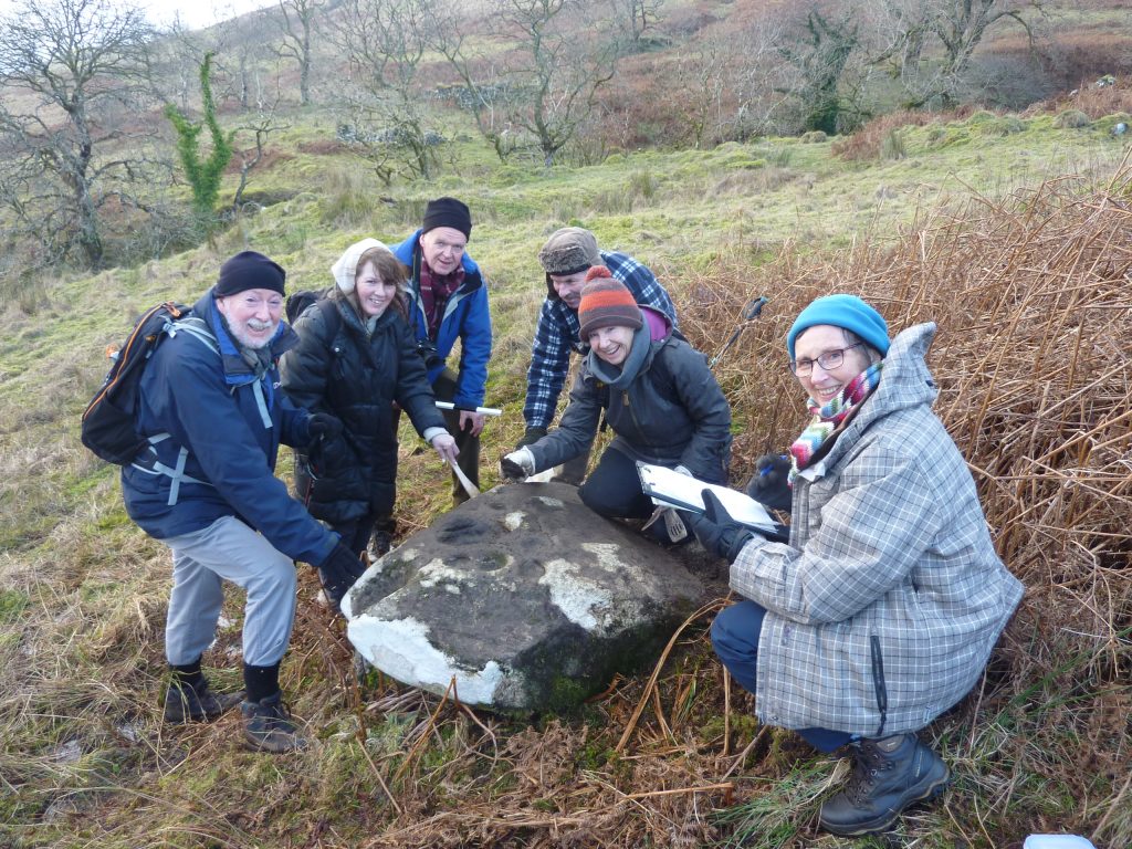 Six people pose and smile around a carved boulder, some with clipboards.