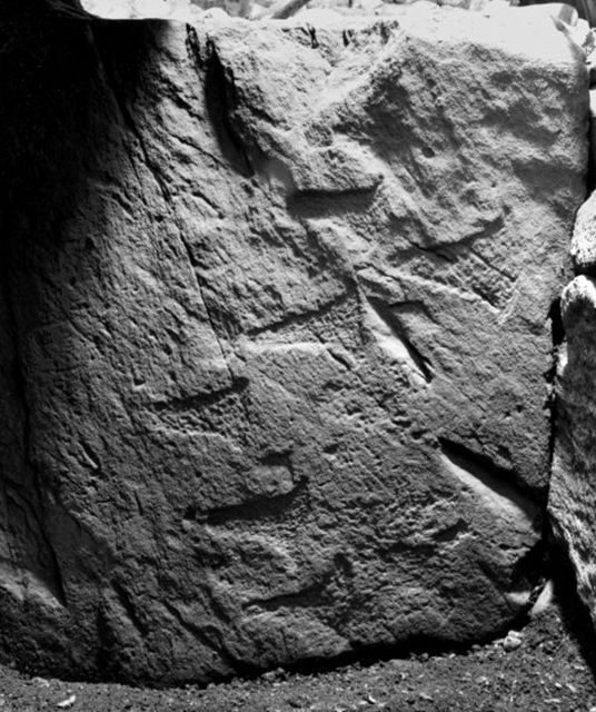 Black and white picture of an area of upright stone with triangular carvings across it.