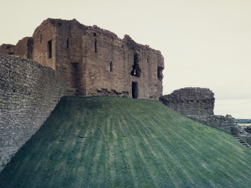 Duffus castle motte canmore_image_SC02113575 A orange-brown building at the top of a sharply-sloping green hill