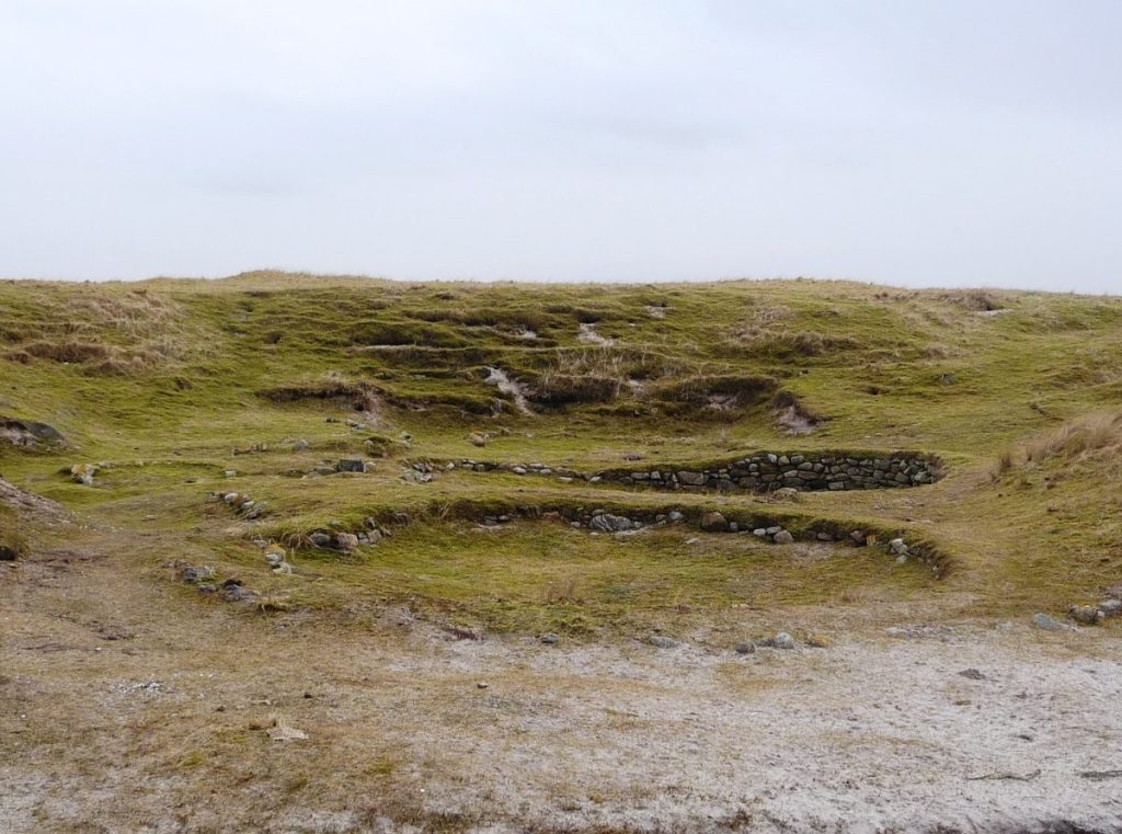 Photo of a grassy hill with multiple prominant stone-lined pits dug into the hillside.