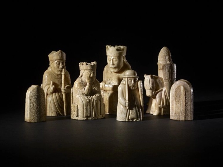 A collection of seven yellow stone coloured chess pieces against a black background. 