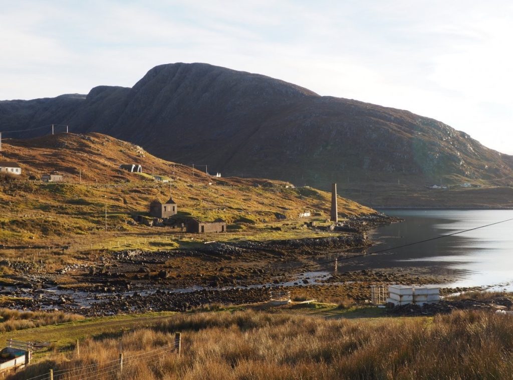 A small hill next to a body of water with pipes and small buildings which make up a post-medieval whaling station