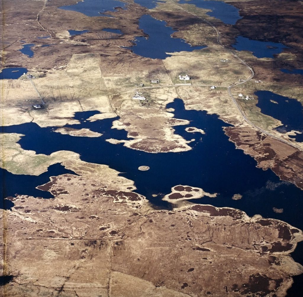 Oblique aerial view of brown land with large water inlets and some small houses punctuating the landscape