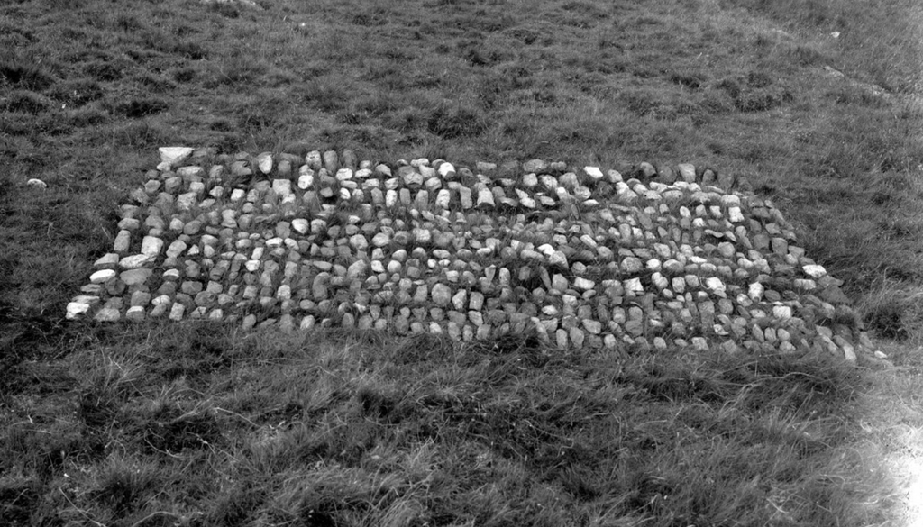 Black and white photograph of a collection of stone artefacts placed in a rectangular shape on grass. 